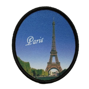 May include: A round, black-bordered patch with a printed image of the Eiffel Tower in Paris, France. The sky is blue and the text "Paris" is printed in white.