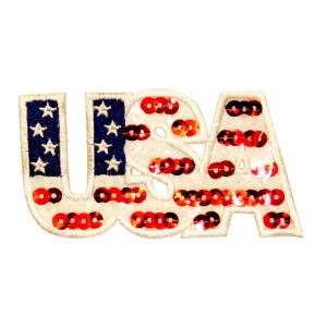 May include: A white felt patch with the word "USA" in red, white, and blue. The letters are outlined in white and filled with red, white, and blue sequins.