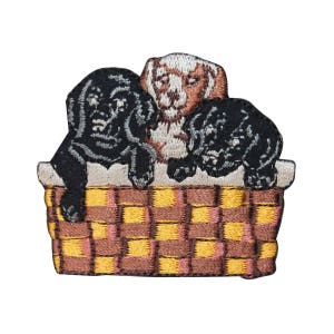 May include: Three embroidered puppies, one brown and two black, are nestled in a brown and yellow checkered basket.