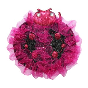 May include: A pink ladybug with black spots and a glittery finish, surrounded by a pink ruffled fabric.