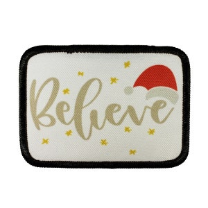 May include: A white fabric patch with a black border. The patch has a gold cursive word "Believe" and a red Santa hat with white trim.