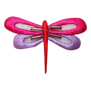 Peut inclure: Une applique de libellule rose et violette avec des accents argentés. La libellule est en tissu et a un centre blanc.