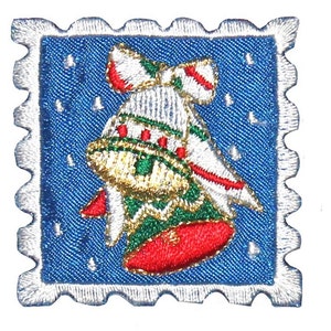 Könnte beinhalten: Eine weiße, rote und grüne Weihnachtsglocke mit Schleife auf blauem Hintergrund mit weißen Schneeflocken. Die Glocke befindet sich in einem weißen Rahmen, der wie eine Briefmarke aussieht.