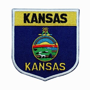 May include: Embroidered patch featuring the state seal of Kansas. The seal depicts a blue sky with a sun, a river, and a grassy hill. The words "Kansas" are written in gold above and below the seal.
