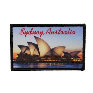 May include: A black framed patch with a colorful image of the Sydney Opera House at sunset. The text "Sydney, Australia" is printed in red at the top of the patch.