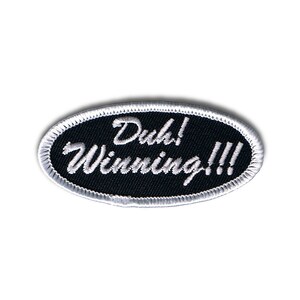 May include: Black oval-shaped patch with white stitching around the edges. The text "Duh! Winning!!!" is embroidered in white on the black background.