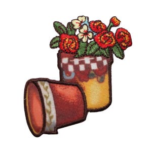 May include: A red and white checked flower pot with a bouquet of red and yellow flowers. The pot is sitting on a brown surface.