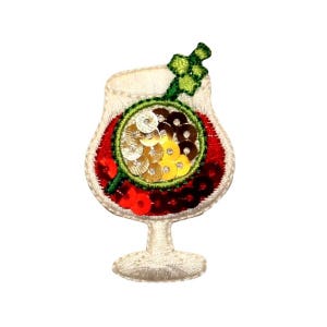 Può includere: Una toppa ricamata bianca di un bicchiere da cocktail rosso con una cannuccia verde e paillettes dorate e gialle all'interno.