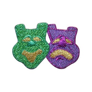 Può includere: Due maschere di stoffa, una verde e una viola, con glitter e ricami dorati. Le maschere sono stilizzate per assomigliare a volti, uno sorridente e l'altro accigliato.