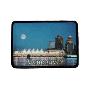 May include: A black and white patch with a photo of the Vancouver skyline at night. The skyline includes the Canada Place convention center, the Harbour Center, and the Harbour Green Hotel. The text "Vancouver" is printed in white at the bottom of the patch.