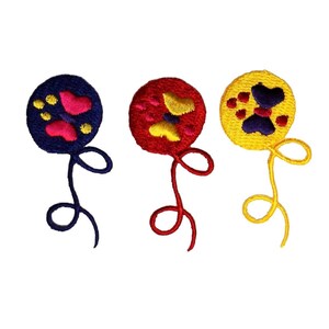 Può includere: Tre toppe ricamate da stirare a forma di palloncino con diversi disegni. Il primo palloncino è blu con una farfalla rosa e impronte di zampe gialle. Il secondo palloncino è rosso con una farfalla gialla e impronte di zampe rosa. Il terzo palloncino è giallo con una farfalla viola e impronte di zampe rosse.