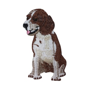 May include: Embroidered patch of a brown and white beagle dog sitting with its tongue sticking out.