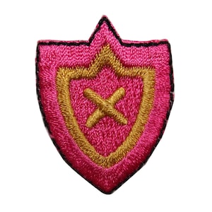May include: A pink embroidered patch with a gold shield and a gold cross inside. The patch has a black outline.