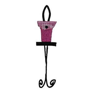 May include: A pink birdhouse with a white trim sits on a black metal stand with a decorative scroll design at the bottom.