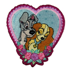 May include: Embroidered patch featuring Lady and the Tramp, a cartoon couple of dogs, in a heart-shaped frame with pink and purple roses.
