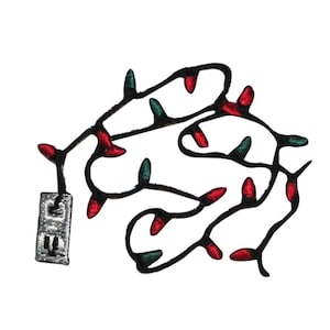 May include: Black and white embroidered patch of a string of Christmas lights with red and green bulbs. The lights are plugged into a wall outlet.