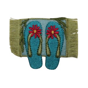 May include: An embroidered patch of a pair of blue flip flops with red flowers on a green and brown rug.