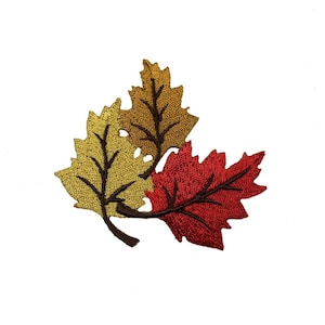 May include: Embroidered leaf applique in shades of gold, brown, and red. The leaves are detailed with intricate stitching, creating a textured appearance. The design features three overlapping leaves, perfect for fall-themed crafts.