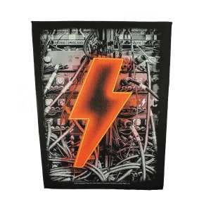 May include: Black and white patch with a large orange lightning bolt graphic. The background is a detailed image of a complex electrical system with wires and connectors.