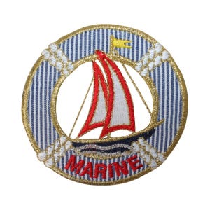 Könnte beinhalten: Ein runder, blau-weiß gestreifter Stoff-Patch mit goldener Umrandung. In der Mitte des Patches befindet sich ein gesticktes rotes Segelboot mit weißem Segel und gelber Flagge. Das Wort "MARINE" ist in Gold unter dem Segelboot gestickt.