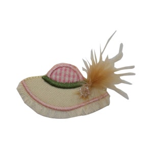 May include: A beige fabric hat with a pink and white checked trim, green trim, and a brown feather accent.