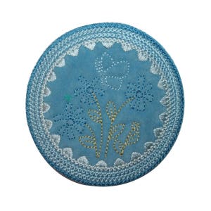 May include: A blue round coaster with a white border and embroidered flowers and a butterfly in the center.