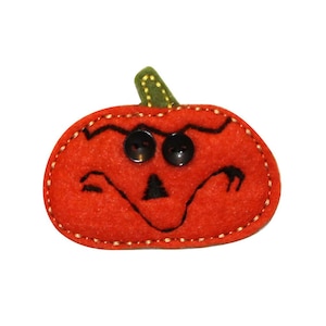 Peut inclure: Une citrouille orange en feutre avec un visage noir cousu et deux boutons noirs pour les yeux. La citrouille a une tige en feutre vert.