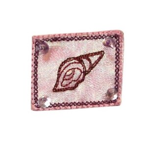 May include: A pink satin patch with a brown embroidered seashell design and silver sequins around the border.