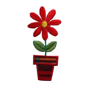 May include: Red embroidered flower with a yellow centre in a red and black plaid pot with green leaves.