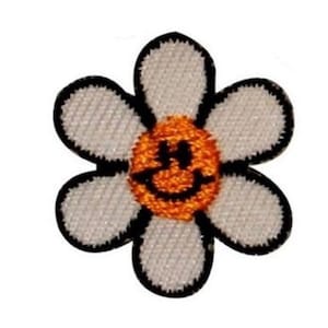 May include: White daisy flower with a smiling orange face in the center. The flower has a black outline.