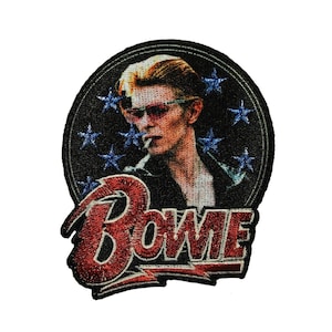 May include: Embroidered patch featuring a portrait of David Bowie in a black leather jacket with sunglasses and a cigarette, against a dark blue background with white stars. The text "BOWIE" is in red and white lettering below the portrait.