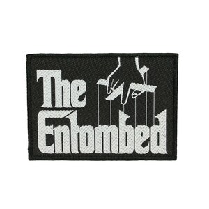 May include: Black and white embroidered patch with the text "The Entombed" and a hand manipulating strings.