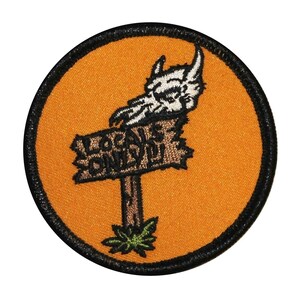 May include: A round orange patch with a black border. The patch features a cartoon skull with horns and a sign that reads "Locals Only".