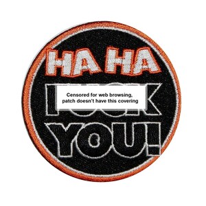 May include: A black and orange round patch with the text "HA HA" in orange and "censored for web browsing, patch doesn't have this covering YOU!" in white.