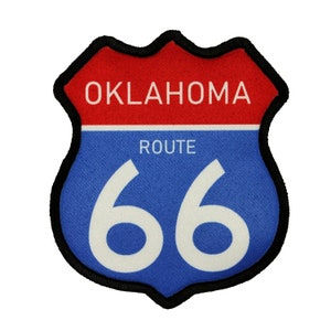 Könnte beinhalten: Ein blaues und rotes Route 66 Schild mit schwarzem Rand. Das Schild ist schildförmig und trägt die Aufschrift "Oklahoma Route 66".