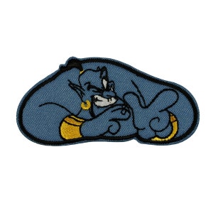 May include: A blue embroidered patch of a genie from Aladdin, with a mischievous expression and a gold band around his waist. The genie is in a sitting position with his arms crossed.