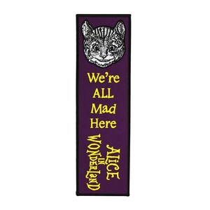 May include: Purple bookmark with a black outline featuring a black and white illustration of the Cheshire Cat from Alice in Wonderland. The bookmark has yellow text that reads "Alice in Wonderland" and "We're All Mad Here."