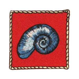 May include: A blue and white embroidered seashell on a red fabric background with a gold rope border.