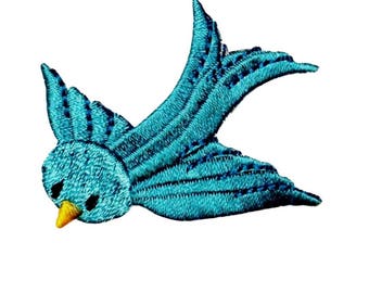 May include: A turquoise blue embroidered bird with a yellow beak, flying with its wings spread out.