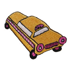 May include: Embroidered patch of a yellow taxi cab with pink and white accents. The patch features black wheels and trim, and a detailed stitched design. The taxi cab is angled slightly to the right, set against a white background.