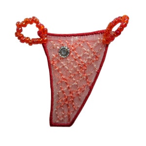 May include: A red and peach-colored thong with a diamond pattern, embellished with a silver gem and beaded orange loops. The edges are outlined in red thread, creating a delicate and intricate design.