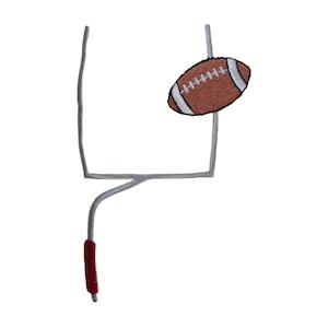 May include: A gray metal football goal post with a brown football in the goal. The football has white laces.