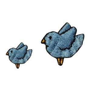 May include: Two blue embroidered bird patches. The larger bird is flying with its wings spread. The smaller bird is perched with its wings folded. Both birds have yellow beaks and feet.