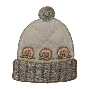 May include: A white knitted hat with a brown pom-pom on top and three brown embroidered flowers on the brim. The hat has a grey knitted band around the bottom.