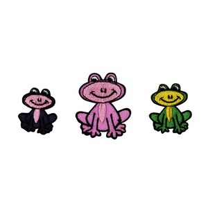 May include: Three embroidered iron-on patches of frogs. The frogs are in different colors: black, pink, and green. The frogs are smiling and have large eyes.