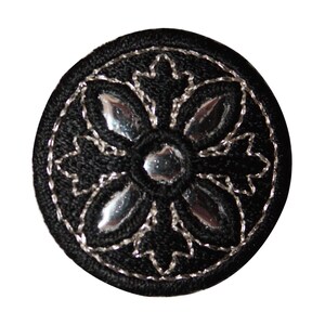 May include: A black round patch with a silver embroidered flower design.