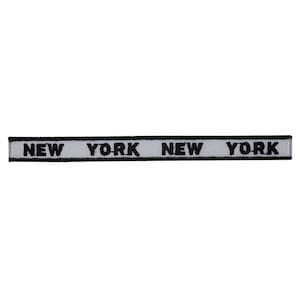 May include: A white fabric ribbon with black text that reads "NEW YORK NEW YORK".