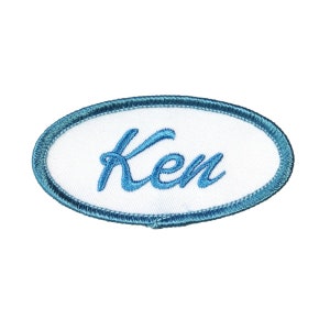 Può includere: Toppa ovale in tessuto bianco con un bordo ricamato blu e il nome "Ken" in lettere corsive blu.