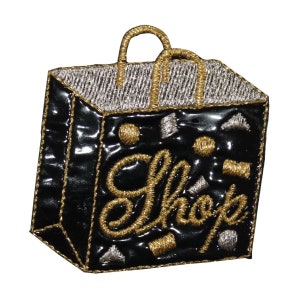 May include: A black embroidered patch shaped like a shopping bag with a gold handle and the word "Shop" in gold lettering. The bag is decorated with gold and silver accents.