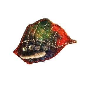 May include: A colorful felt leaf brooch with a rainbow pattern and silver sequins. The leaf is stitched with a dark brown thread and has a red border.